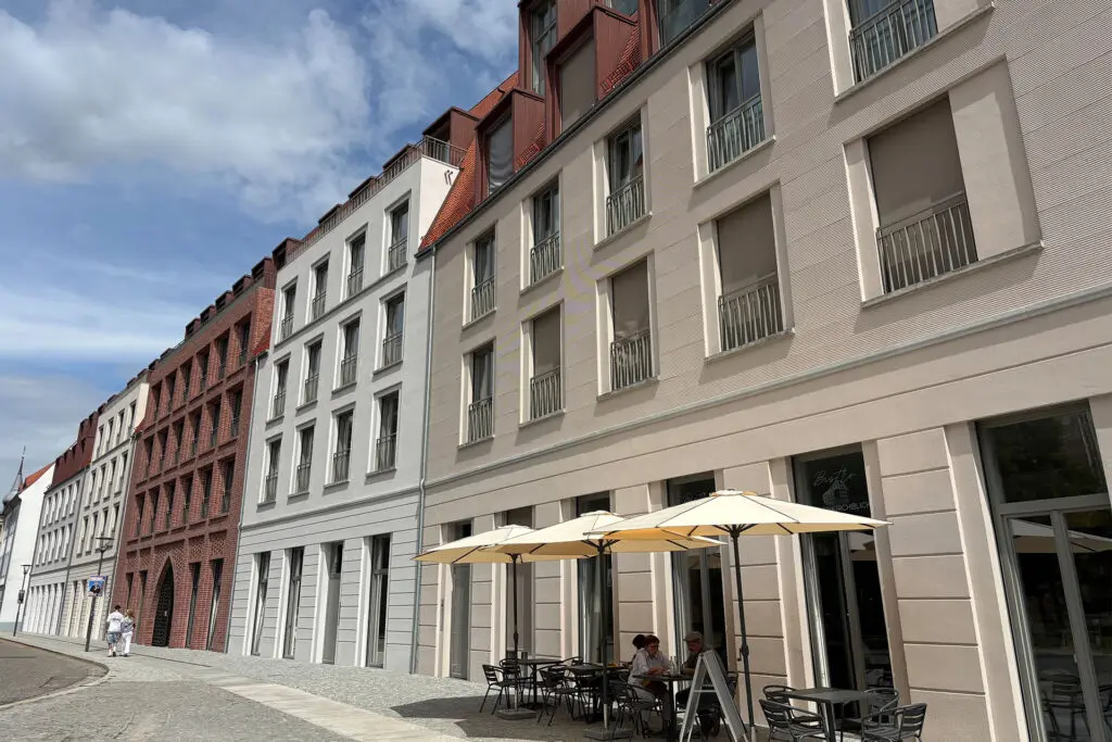 Außenansicht eines Bistros mit Tischen und Sonnenschirmen vor Gebäuden. Marienkirchblick.