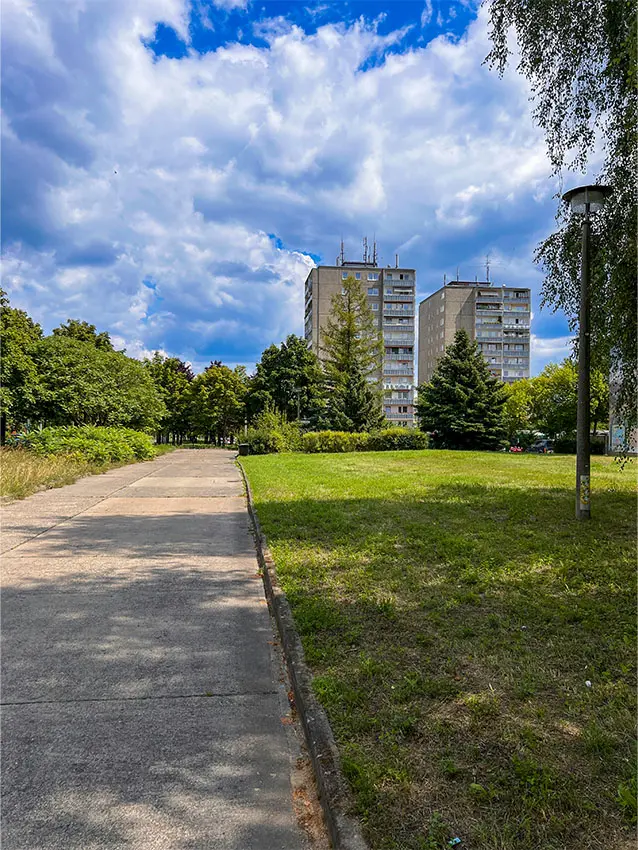 Neuberesinchen Aurorahügel: Weg führt zu zwei Hochhäusern durch Grünanlage unter blauem Himmel.