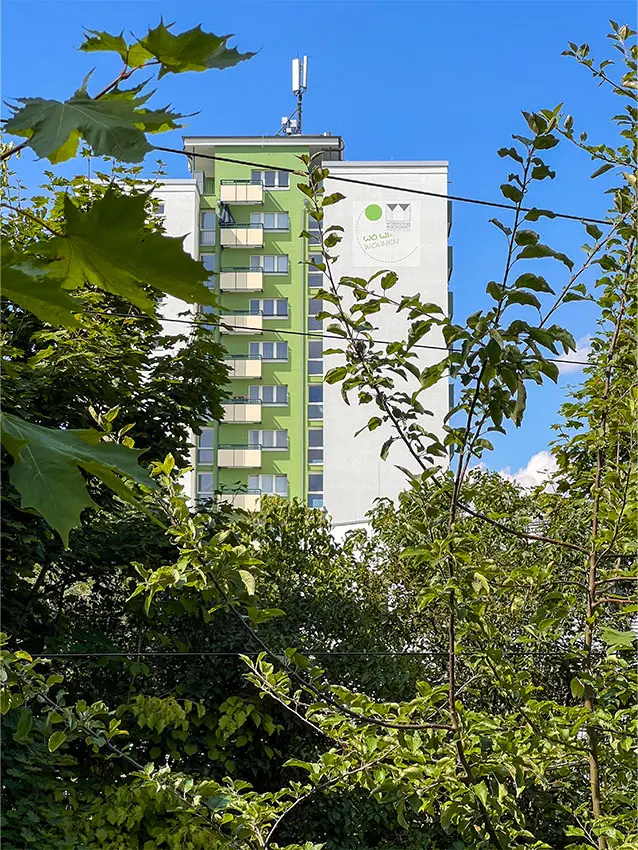 Mehrgeschossiges Wohngebäude, teilweise von Bäumen verdeckt, mit Antenne auf dem Dach.