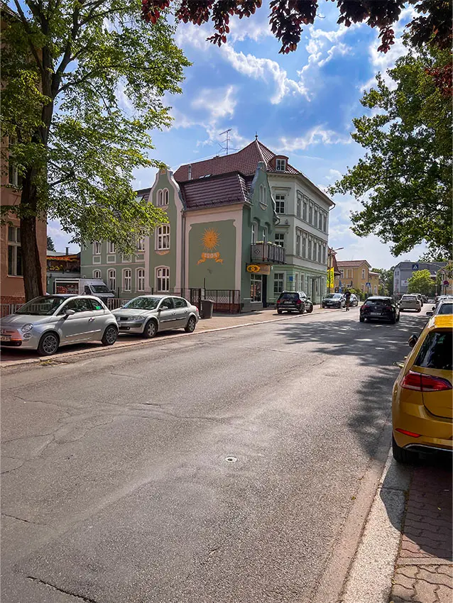 Straße mit geparkten Autos und Gebäuden im Stadtteil. Fassade mit Sonnensymbol.