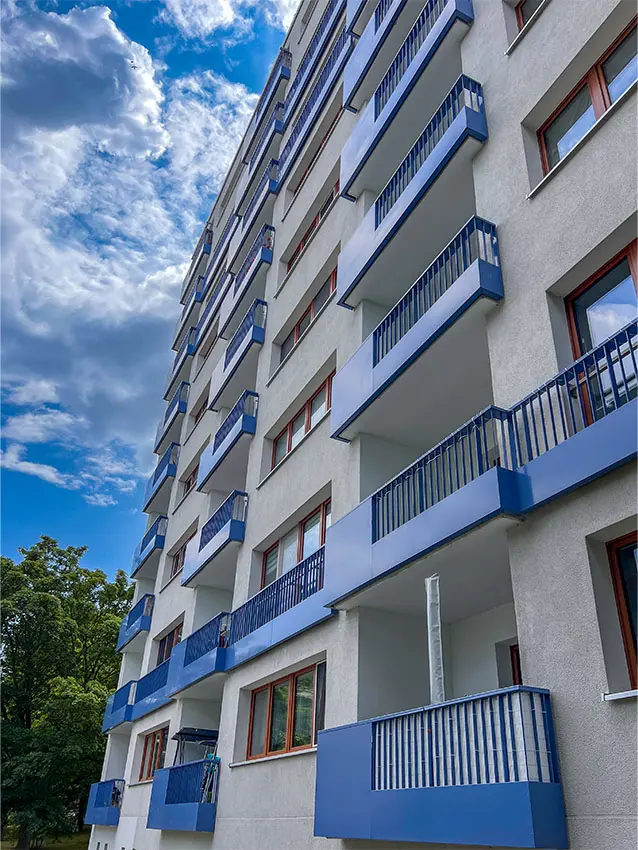 Mehrfamilienhaus Fassade mit blauen Balkonen und Fensterrahmen unter blauem Himmel.
