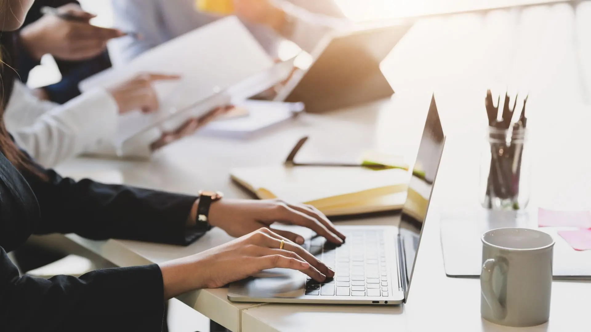 Büro Gewerbe: Frau tippt auf Laptop, Büroarbeit im Team, mit Dokumenten und Tasse.