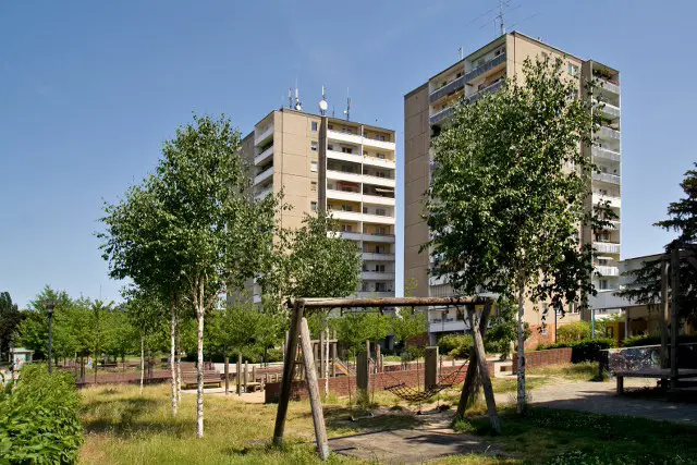 neuberesinchen_7070_umfeld Neuberesinchen Startseite: Zwei hohe Wohngebäude mit Balkonen hinter Bäumen und einer Schaukel im Vordergrund.