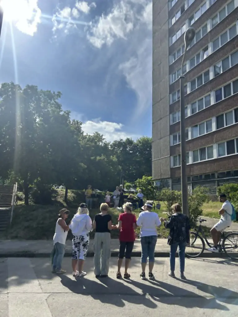 Menschen stehen bei Treppenhausmusik 2027 auf dem Platz, während im Hintergrund Musiker vor einem hohen Wohnblock spielen