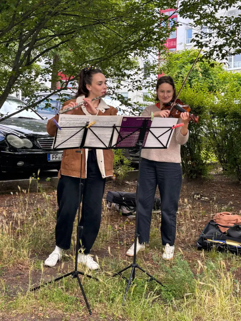 Zwei Musikerinnen spielen bei Treppenhausmusik 2027 im Freien Flöte und Geige vor ihren Notenständern auf einer Wiese