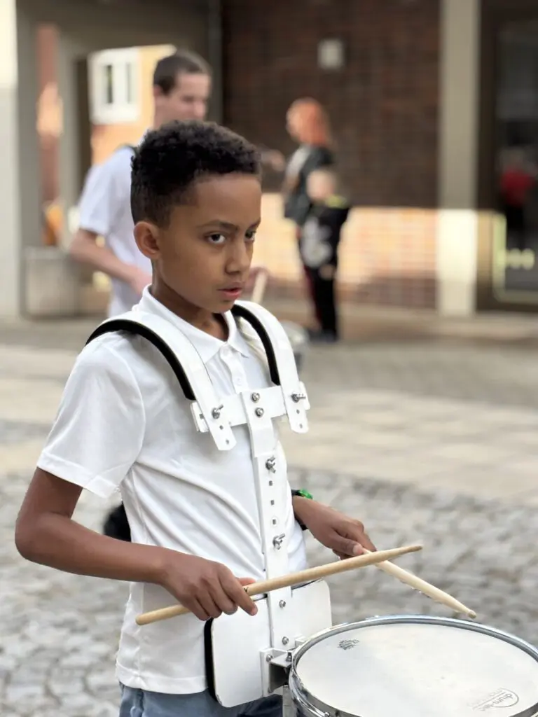Fokussierter Junge in weissem Poloshirt traegt bei Treppenhausmusik 2027 eine Snare Drum und hält zwei Schlagzeugstoecke