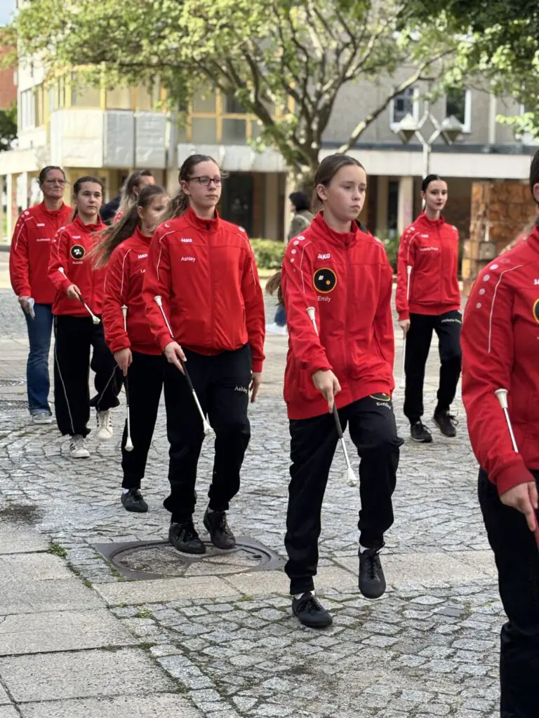 Mitglieder einer Tanzgruppe in roten Jacken gehen bei Treppenhausmusik 2027 mit Schlagstöcken über das Kopfsteinpflaster