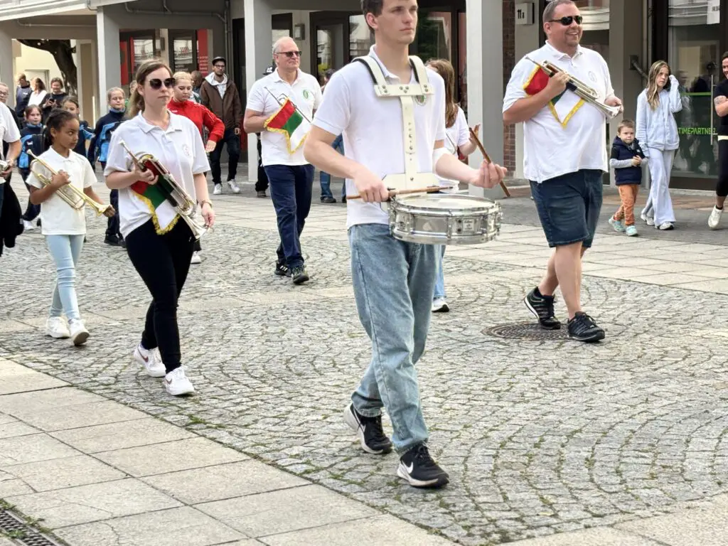 Musikkapelle in weissen Poloshirts marschiert bei Treppenhausmusik 2027 mit Trommeln und Trompeten ueber gepflasterte Wege