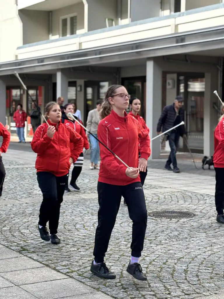 Mehrere junge Frauen in roten Jacken und schwarzen Hosen marschieren bei Treppenhausmusik 2027 mit Stäben in der Hand