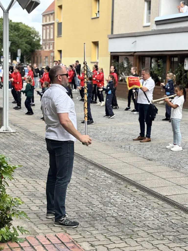 Ein Mann mit Stab leitet bei Treppenhausmusik 2027 eine Musikgruppe mit Trompetenspielern an auf einem gepflasterten Platz