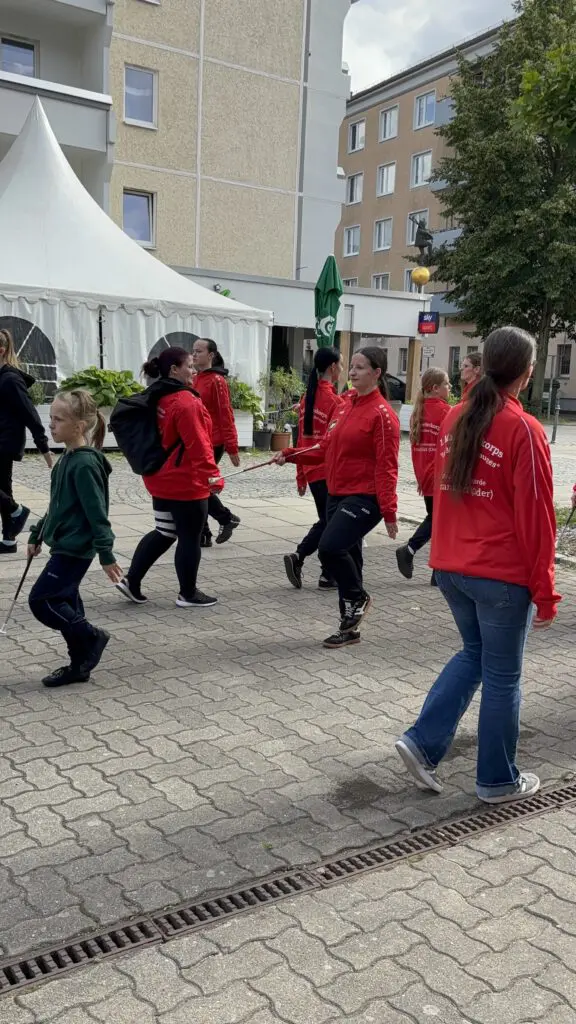 Marschierende Formation in roten Jacken bei Treppenhausmusik 2027 mit einer jungen Person im grünen Kapuzenpullover vorne