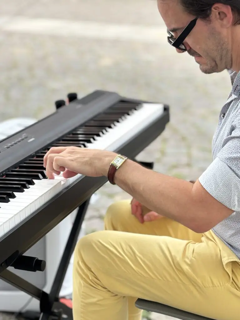 Ein Mann mit Brille in gelber Hose spielt Keyboard fuer Treppenhausmusik 2027 mit Blick auf die Tasten