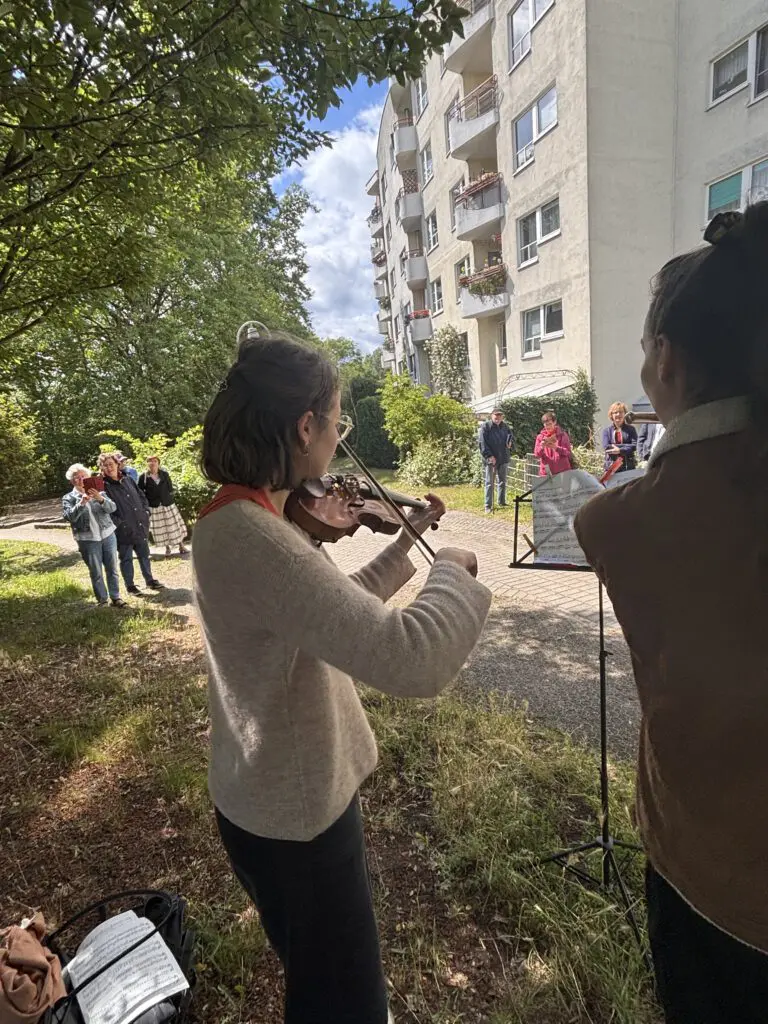 Geigerin in heller Strickjacke spielt bei Treppenhausmusik 2027 unter freiem Himmel vor einem Wohnhaus
