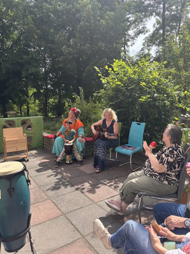 Frauen musizieren bei Treppenhausmusik 2027 auf Akustikgitarre und Trommeln im Garten bei sonnigem Wetter