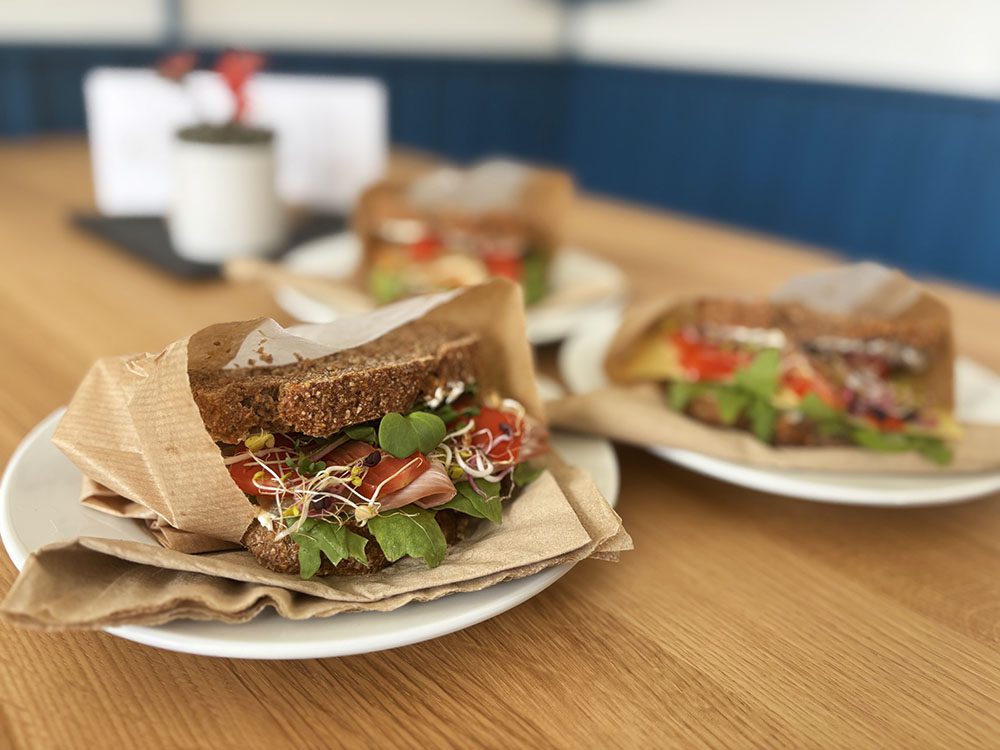Marienkirchblick-Bistro: Mehrere appetitliche Stullen, serviert auf Tellern mit Papier, auf einem Holztisch.