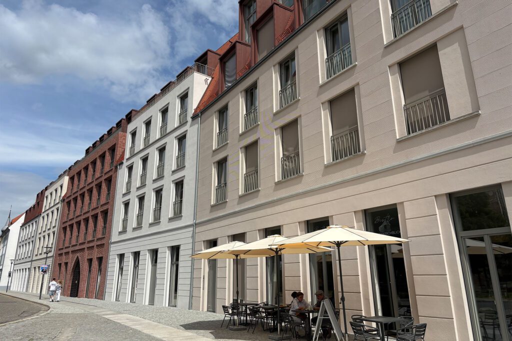 Außenansicht eines Bistros mit Tischen und Sonnenschirmen vor Gebäuden. Marienkirchblick.