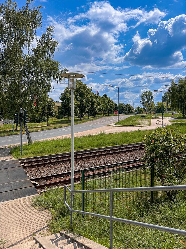 Neuberesinchen: Blick auf Gleise, Straße und blauen Himmel mit Wolken. Grünflächen und Bäume.