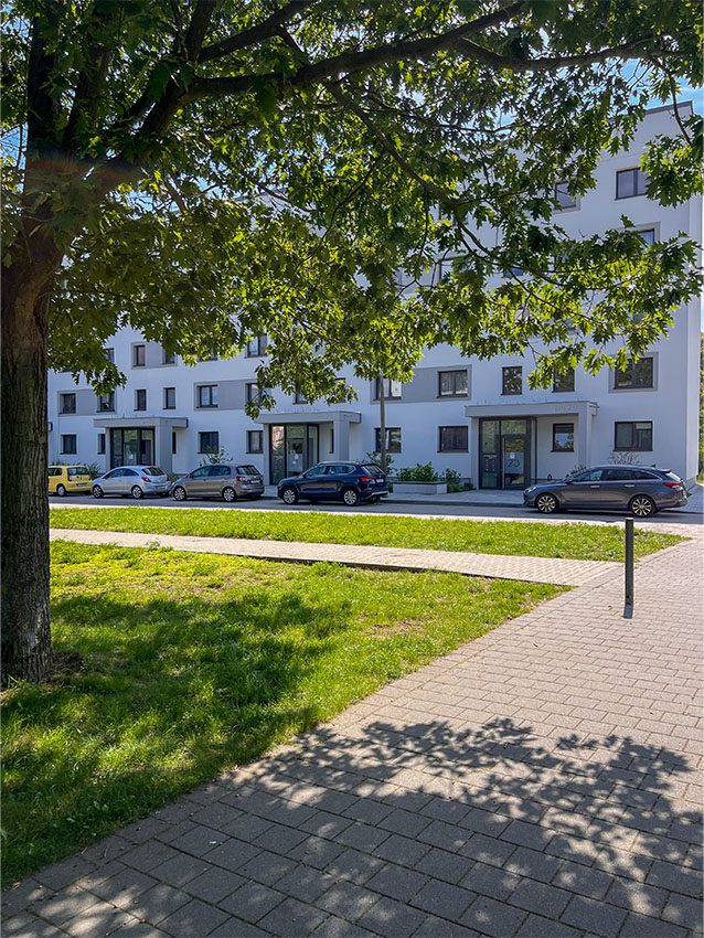 Mehrfamilienhaus mit Autos, Rasen und Baum. Wohngebiet mit Fassade und Grünflächen.
