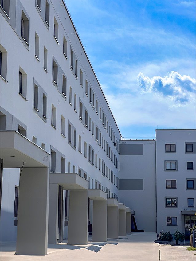 WOWI FFO Stadtteil Süd: Fassade eines modernen, hellen Wohngebäudes mit vielen Fenstern und Säulen vor blauem Himmel.