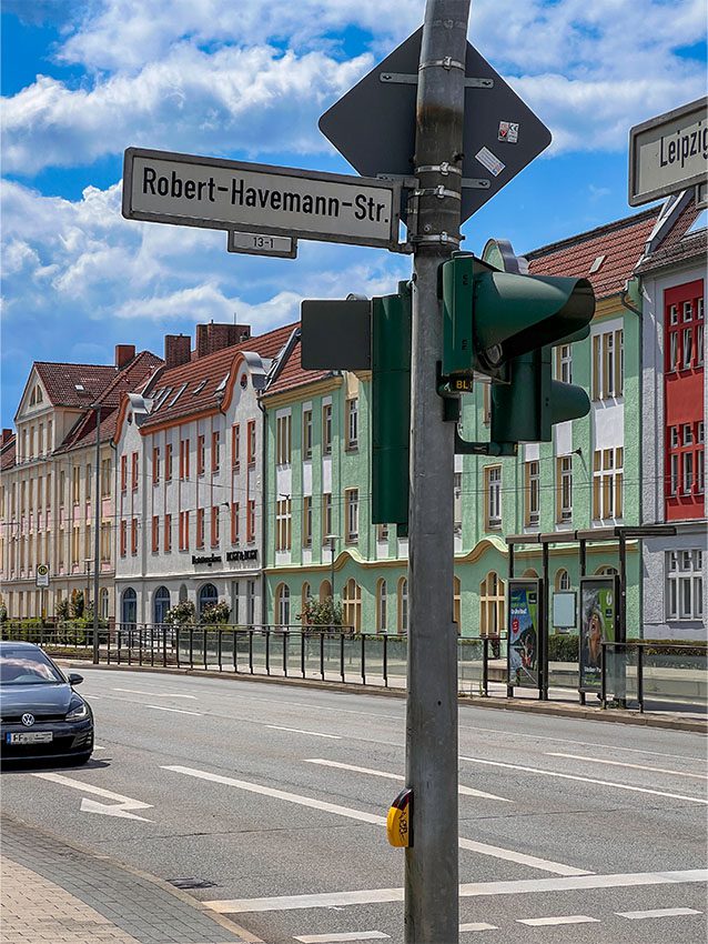 Straßenschild Robert-Havemann-Str., Ampel und Gebäude im Hintergrund.