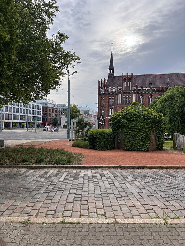 Stadtteil-Zentrum: Gebäude mit Turm, Grünflächen und Pflastersteinen.