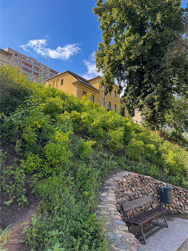 Gelbes Gebäude auf Hügel, Bank im Vordergrund. Stadtteil-Zentrum Bruno-Peters-Berg.