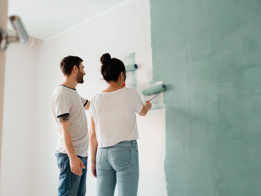 DIY-Wohnung: Paar streicht Wand mit Farbroller. DIY-Ideen für Wohnungen.