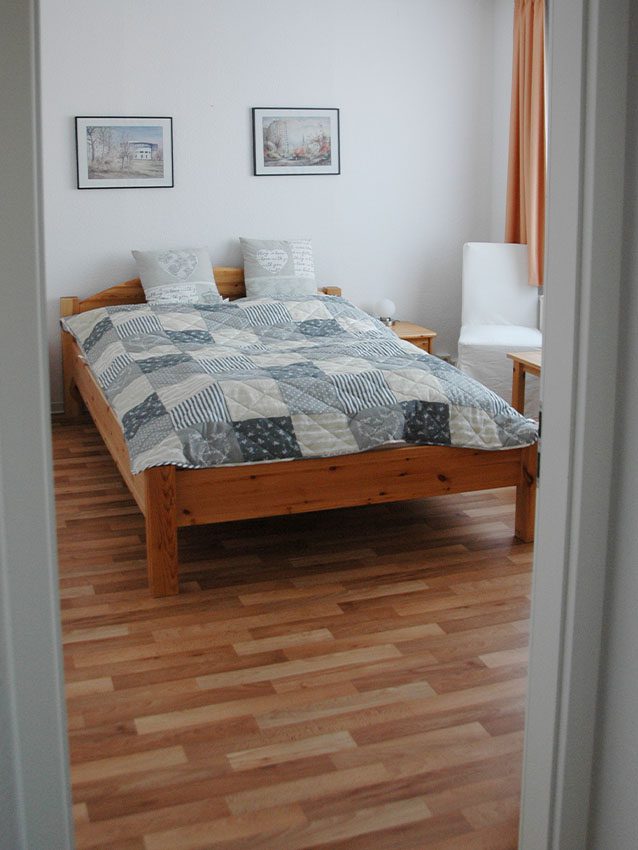 Möbliertes Wohnen: Bett mit Patchwork-Decke, Kissen und Bildern an der Wand.