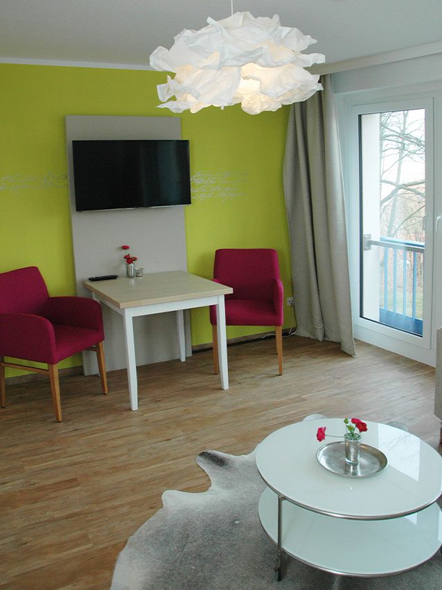 Möbliertes Wohnen: Zimmer mit Tisch, Stühlen, TV und Lampe.