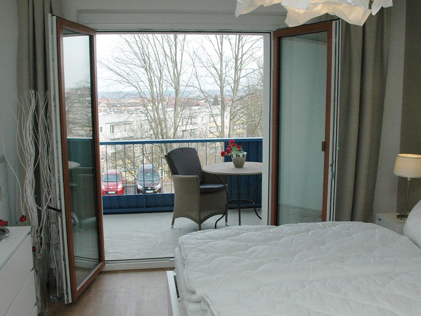 Möbliertes Wohnen: Zimmer mit Bett und Balkon mit Tisch und Stuhl.