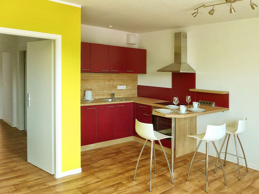 Möbliertes Wohnen: Küche mit Esstheke, roten Schränken und weißen Barhockern.