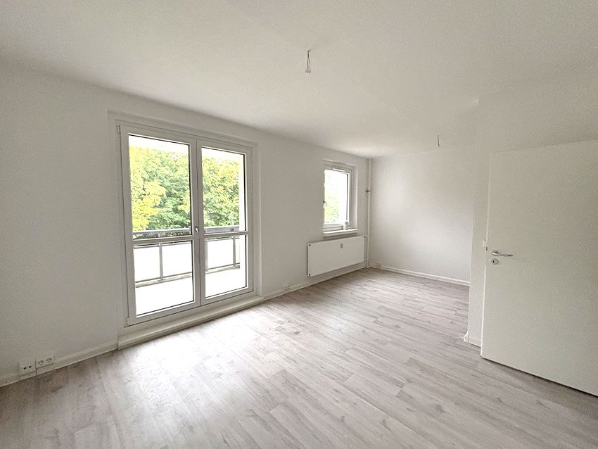 WOWI Juri-Gagarin-Ring: Helles, leeres Zimmer mit Fenster, Tür und Laminatboden.
