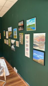 Wandatelier: Gemäldeausstellung mit Talenten. Verschiedene Kunstwerke, Landschaften und abstrakte Malerei an grüner Wand.