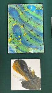 Wander-Atelier der Talente: Gerahmtes abstraktes Kunstwerk in Blau, Grün und Gelb. Ein weiteres Kunstwerk darunter.