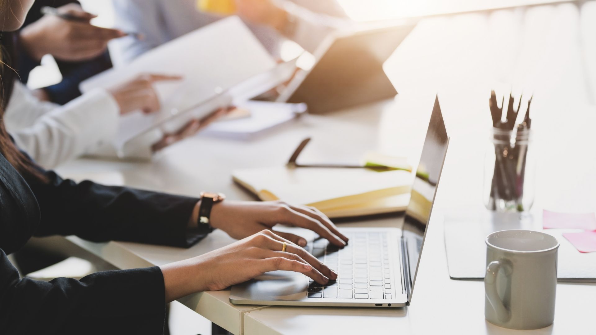 Büro Gewerbe: Frau tippt auf Laptop, Büroarbeit im Team, mit Dokumenten und Tasse.