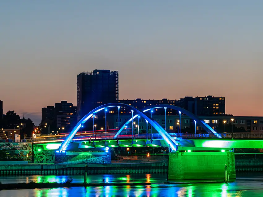 Was-uns-wichtig-ist Was uns wichtig ist: Beleuchtete Brücke mit blau-grüner Beleuchtung über Wasser, im Hintergrund die Skyline. Reflektiert im Wasser.