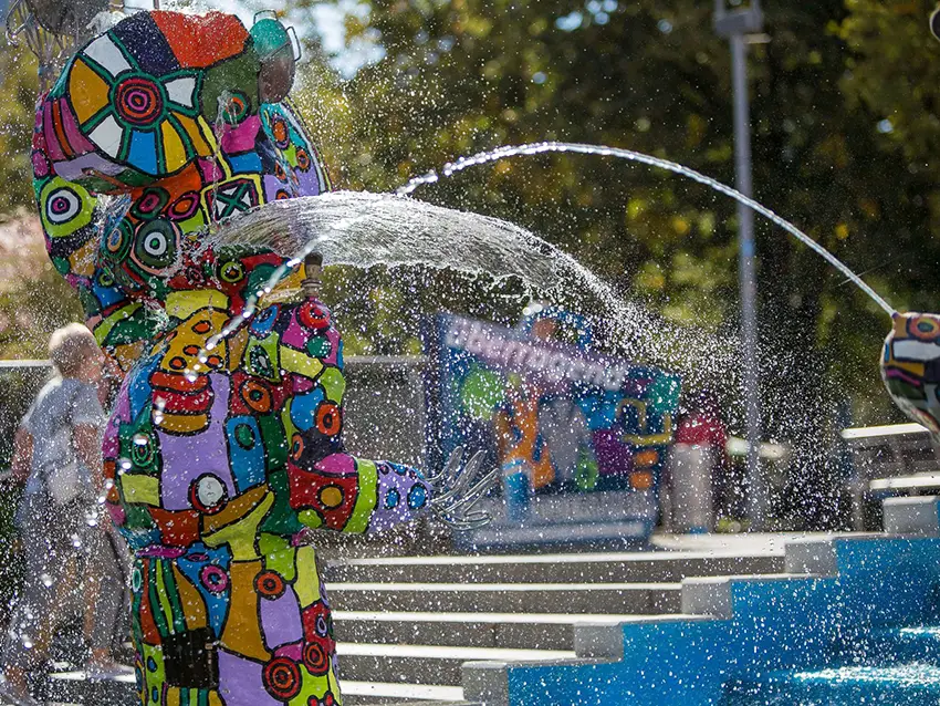 Farbenfrohe Zentrum-Skulptur mit Wasserspiel. Die abstrakte Kunstfigur sprüht Wasser, belebt durch lebendige Muster.
