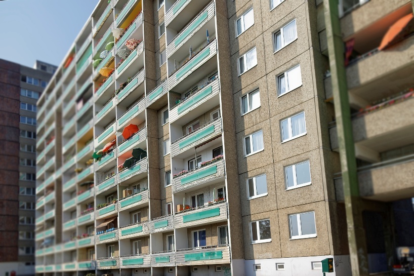 Dr-Salvador-Allende-Hoehe-vor-sanierung Dr-Salvador-Allende-Hoehe vor Sanierung: Fassade eines Mehrfamilienhauses mit Balkonen, Sonnenschirmen und Fenstern. Investition in Wohnzukunft.