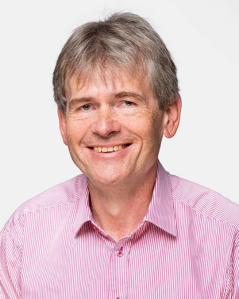 Draemel Kontakt Draemel: Porträt eines lächelnden Mannes mit grauem Haar und gestreiftem Hemd, aufgenommen vor einem neutralen Hintergrund.