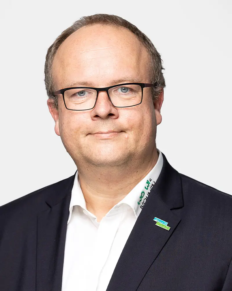 Eckardt Kontakt Eckardt: Porträt eines Mannes mit Brille, Anzug und einem Abzeichen am Revers. Freundlicher Gesichtsausdruck.