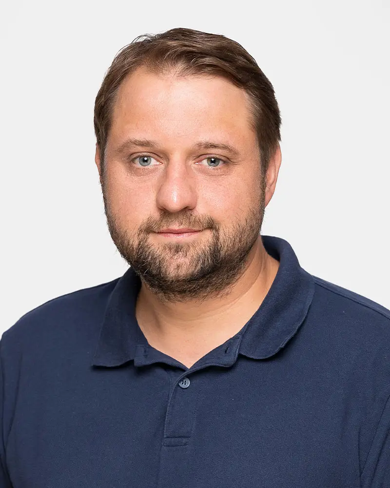 Mosig Kontakt Mosig: Porträt eines Mannes mit braunen Haaren und Bart, der ein blaues Poloshirt trägt. Freundlicher Gesichtsausdruck.