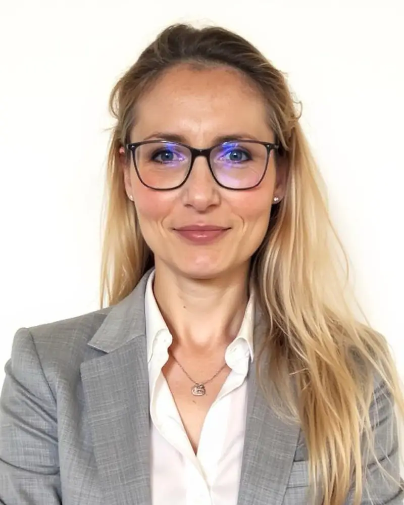 Ullmann Kontakt Ullmann: Porträt einer Frau mit Brille, blonden Haaren, Blazer und Bluse vor einem hellen Hintergrund.