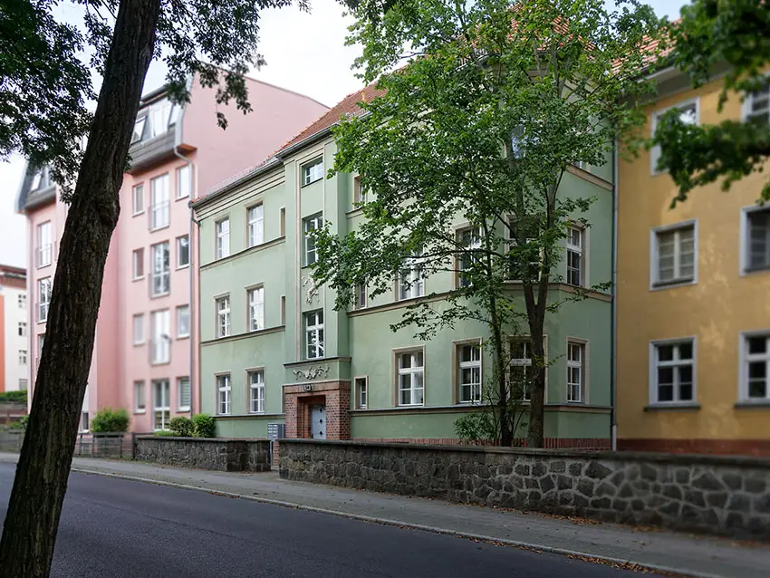 WOWI-FFO-Stadtteil-Altberesinchen WOWI-FFO-Stadtteil-Altberesinchen: Mehrfarbige Wohnhäuser mit Bäumen und einer niedrigen Steinmauer im Stadtteil.